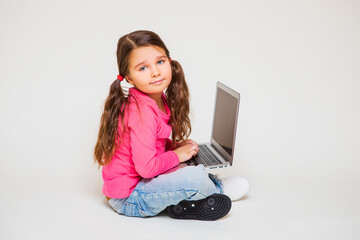 Cute kid girl smiling sitting on light floor uses gray laptop    