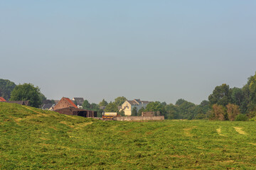 Fototapeta na wymiar Freshly mown farmland in a sunny hilly landscape with a farm and houses under a blue sky.