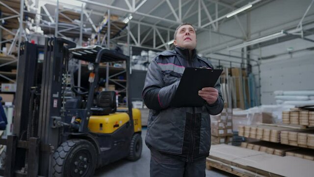 Concentrated professional warehouse worker filling in bill of lading standing in industrial storage indoors writing with pen in document. Portrait of focused expert shipping agent preparing paperwork