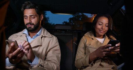 Mixed-race woman and indian man woman texting on smartphone a sitting on backseat in taxi car