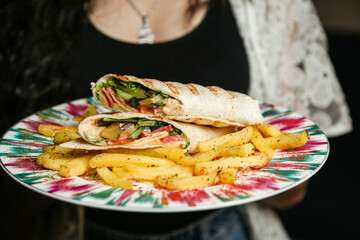 chicken roll in a pita with fresh vegetables, cream sauce and french fries on wooden background.