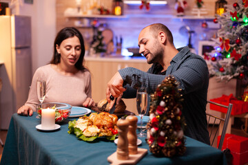Married happy couple sitting at dining table in xmas decorated kitchen enjoying christmas winter dinner. Romantic cheerful happy celebrating christmas holiday. Santa-claus wintertime