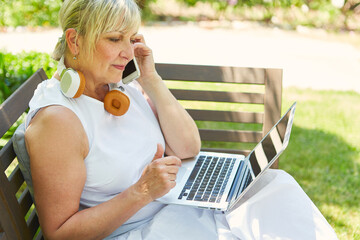 Frau im Garten am Laptop telefoniert mit Smartphone