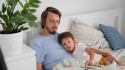 beloved father reads a book to his son in a white bed
