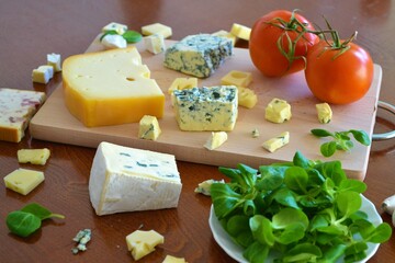 Assortment of cheeses on a cutting board and a wooden table