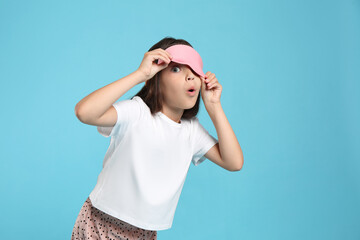 Cute girl wearing pajamas and sleeping mask on light blue background