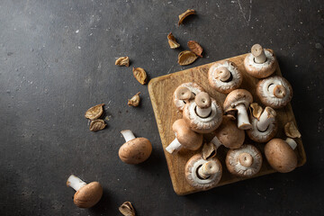 Fototapeta na wymiar Raw portobello mushrooms on wooden board with autumn leaves in the dark background.Copy space