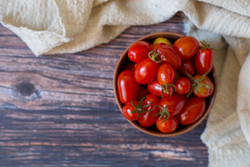 Pickled cherry tomatoes in clay plate on wooden background, top view