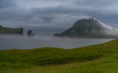 Mystical foggy lansdcapes along the coast of Vagar Island, Faroe Islands with the Skar&eth;s&aacute;fossur waterfall in the foreground