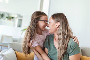 Close up of sweet pretty daughter cuddling with her young mother. Lovely mother embracing her cute daughter on the sofa at home.