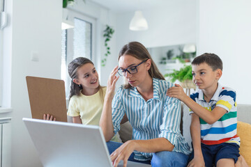 Woman working from home during quarantine with her little son and daughter on couch and screaming, demanding attention