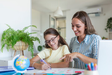 Cute girl with mother doing homework at home. A mother helps her little daughter to do her homework for the school. Education and family concept - obrazy, fototapety, plakaty