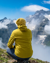 A tourist in a yellow jacket and a knitted hat on the top of high rocks. Sports and active life concept
