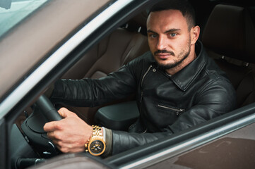 Portrait of handsome young man driving modern car. Guy driver wearing casual clothes and gold watch.