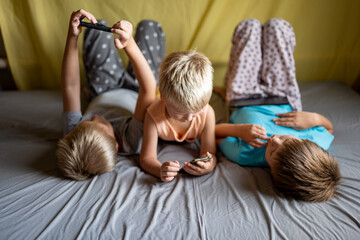 three funny boys lie on couch and play on smartphones and tablets. Children are passionate about game and their devices