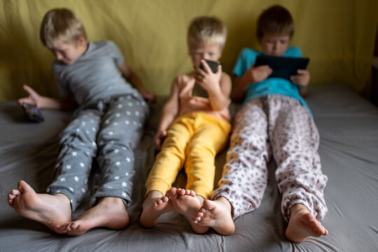 three funny boys lie on couch and play on smartphones and tablets. Children are passionate about game and their devices
