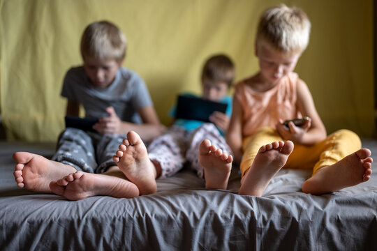 three funny boys lie on couch and play on smartphones and tablets. Children are passionate about game and their devices