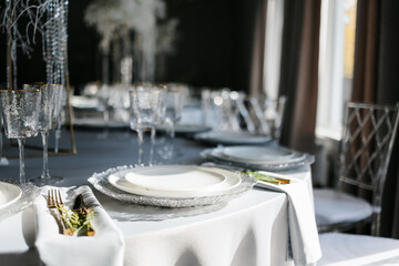 glass glasses and white plates. table setting in the interior of the restaurant. The decor of the festive table. In gray-silver tones with gold cutlery. Luxury wedding, party, birthday.