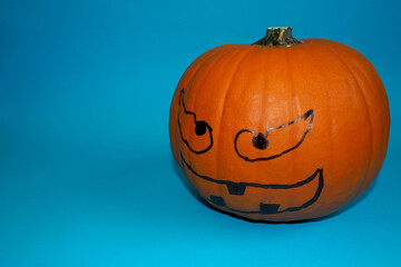 halloween. a pumpkin with a marker drawn on its face, for the holiday, stands on a blue background. side view