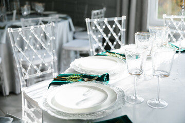 glass glasses and white plates. table setting in the interior of the restaurant. The decor of the festive table. In gray-silver tones with gold cutlery. Colored napkins.
