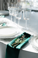 gold-colored devices on napkins of different colors. Grey, red and green napkin. Plates and glasses are placed on the table. Festive table decor