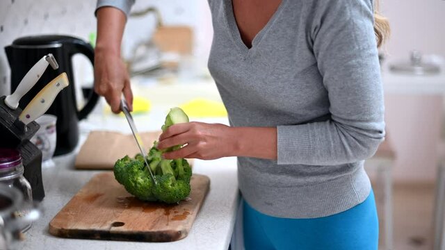 Woman cutting green broccoli at the kitchen
