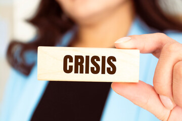 CRISIS inscription on the texture of wooden block. A business women holds a block in his hand. An inscription on a financial, business or economic theme.