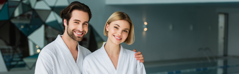 Cheerful man in bathrobe hugging girlfriend in spa center, banner