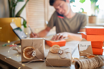 Young millennial worker packing Christmas gift boxes for clients, family small business. New Year...
