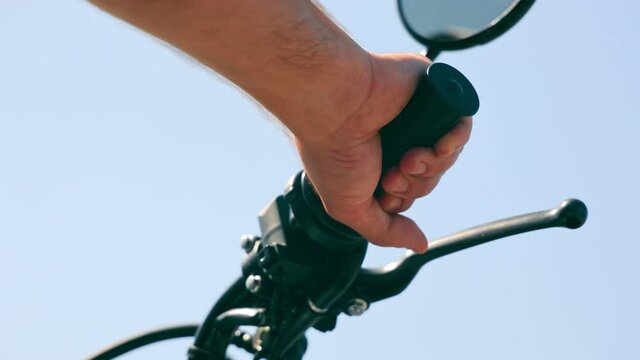 Close up of a man's mitten hand on the handlebars of a motorcycle. Motorcyclist pulls the gas trigger on a background of blue sky.