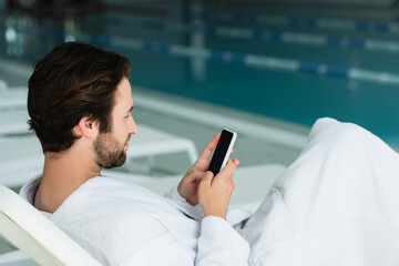 Side view of man using cellphone on deck chair in spa center