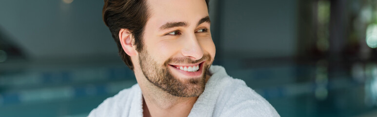 Obraz premium Smiling man in white bathrobe looking away in spa center, banner
