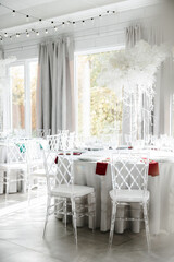 Round table with transparent plastic chairs. Flower arrangement in the center of the table. The interior of the restaurant for a wedding dinner. A round banquet table is set. The concept of catering. 
