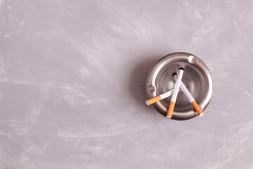 Metal ashtray and pack of cigarettes on stone background