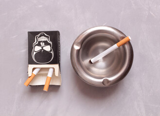 Metal ashtray and pack of cigarettes on stone background