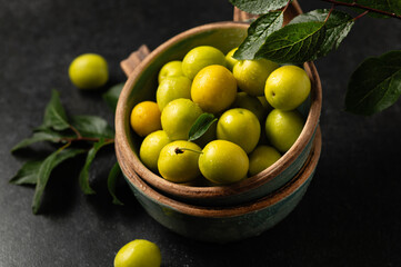 yellow freshly torn cherry plum with green leaves in ceramic cups on a gray background, close-up