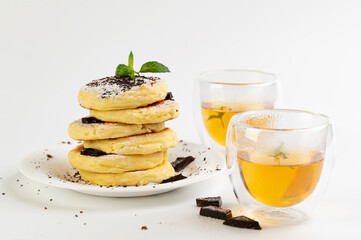 curd cakes, curds on a white dessert plate with chocolate and mint, green tea in glass cups
