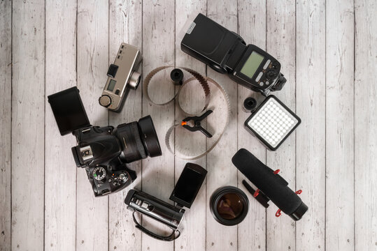 film camera with a digital video camera and a microphone are lying on a table with a lens and a film in a coil on a wooden table