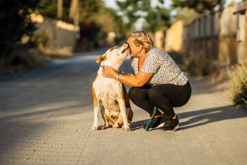 Dog kissing a woman while sitting in an unpaved street