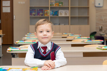 A first-grader boy at a desk with textbooks and notebooks in the classroom on the day of knowledge on September 1 at school at the lesson. Selective focus. Close-up