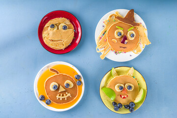 Creative homemade Halloween pancakes for breakfast, in form of funny monsters, ghost, bat, witch. With traditional trick or treat sweets, candy and decorations, top view on colorful blue background