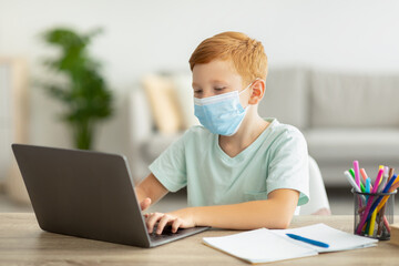 Redhead boy schooler in face mask using laptop, home-schooling concept