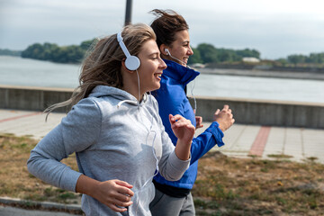 Two young happy and self loved woman the best friends jogging and running outdoor near the river for health life doing bodyweight workout and training by jog together while they listening to music