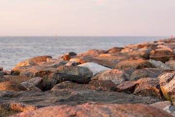 Rocks on the beach at sunset. Sun is setting over the rock pier. Breakwater at sea coast during pink sundown at calm evening.