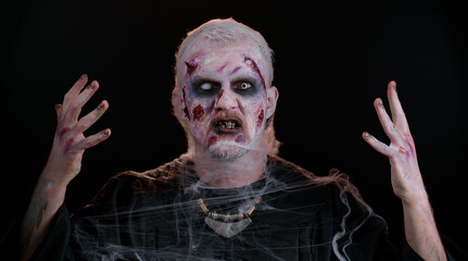 Portrait of sinister man in carnival costume of Halloween crazy zombie with bloody wounded scars face trying to scare isolated on black room. Horror theme of cosplay wounded undead, beast, monster