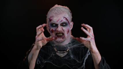 Portrait of sinister man in carnival costume of Halloween crazy zombie with bloody wounded scars face trying to scare isolated on black room. Horror theme of cosplay wounded undead, beast, monster