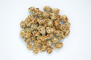 Roasted peanuts in sugar with sesame seeds on a white plate top view. Peanuts in honey caramel and sprinkled with sesame seeds. Sweet snacks with nuts. 
