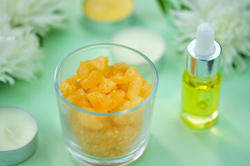 Sea salt in a glass with the smell of orange and tea oil, candles on a green background. The topic of relaxation, bathing, evening relaxation. Sea salt and essential oil close-up. 