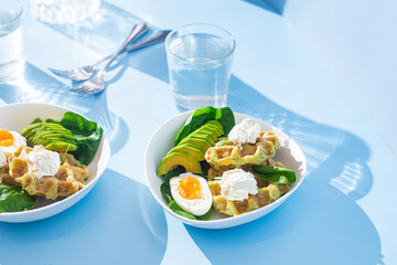 Belgian waffles with cream cheese, egg and avocado in a white plate. Healthy breakfast