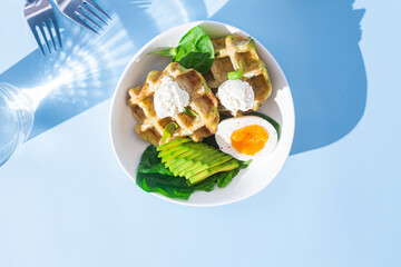 Belgian waffles with cream cheese, egg and avocado in a white plate. Healthy breakfast